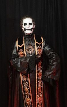 a man in a costume with a mask and black cape standing next to a black curtain