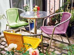 three colorful chairs and a table on a brick patio with flowers in the foreground