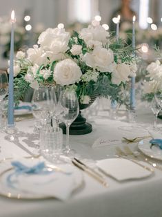 the table is set with white flowers and blue place settings for an elegant dinner party