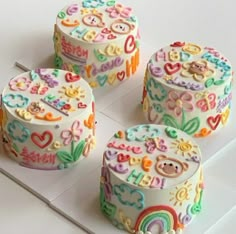 four decorated birthday cakes sitting on top of a white table with rainbows and hearts