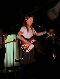 a woman playing an electric guitar while standing in front of a microphone and other people