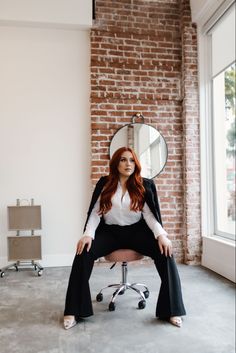 a woman sitting on top of a chair in front of a brick wall with a mirror