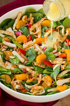 someone pouring dressing into a salad with oranges, spinach and chicken in it