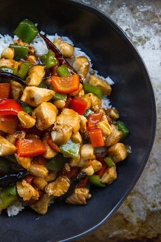 a black bowl filled with rice and chicken stir fry on top of a wooden table