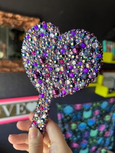 a hand holding a heart shaped brooch in front of a wall with other items on it