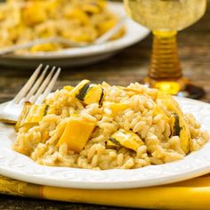 two white plates with rice and squash on them next to a glass of wine in the background