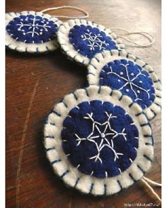 three blue and white snowflake ornaments are hanging on a wooden table with twine