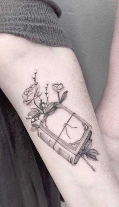 a woman's arm with a book and flowers tattoo on the left inner forearm