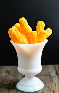 a white bowl filled with cheetos sitting on top of a wooden table next to a black wall