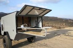 an off - road camper is parked on the side of a dirt road with its door open