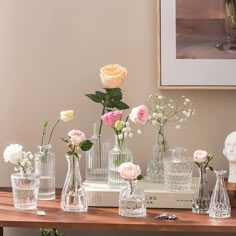 several vases with flowers on a table in front of a framed photo and a busturine