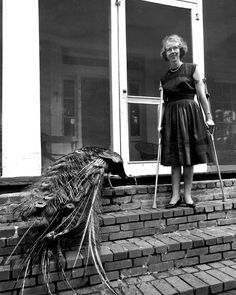 an old black and white photo of a woman standing on the steps with a peacock