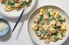 two plates of pasta with meat and spinach on them next to a bowl of grated parmesan cheese