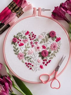 a heart - shaped embroidery on a pink hoop with flowers and scissors next to it