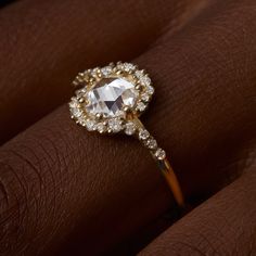 a woman's hand with a diamond ring on her left hand, and the center stone is surrounded by smaller diamonds