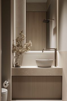 a bathroom sink sitting under a mirror next to a toilet and a vase with flowers