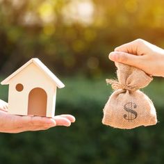 two hands holding a small house and money bag