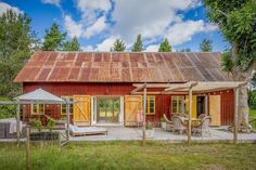 an old red barn is surrounded by trees and lawn chairs with umbrellas on the porch