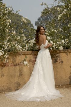 a woman in a white wedding dress standing next to some bushes and flowers with her back turned towards the camera