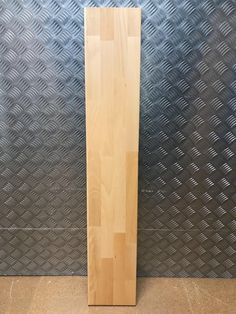 a tall wooden object sitting on top of a metal floor next to a diamond pattern wall