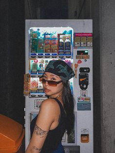 a woman wearing sunglasses and a bandana standing in front of a vending machine