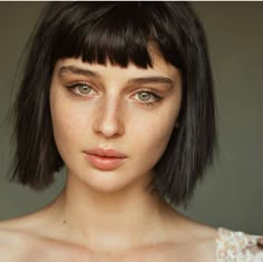 a close up of a woman with short black hair and brown eyes wearing a white dress