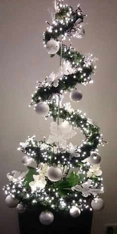 a christmas tree with lights and ornaments on it's branches in a black pot