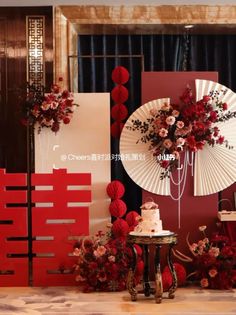 a table topped with a cake and flowers next to tall red wall dividers covered in paper fans