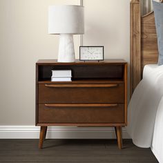 a night stand with a clock on it next to a bed