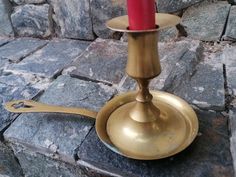 a small brass candle holder with a red candle on it's side and some rocks in the background