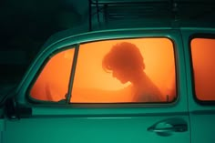 a woman is looking out the window of a green car with orange light coming through it