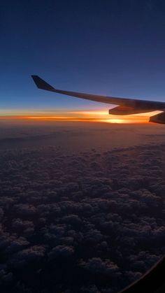 the wing of an airplane as it flies through the sky at sunset or dawn with clouds below