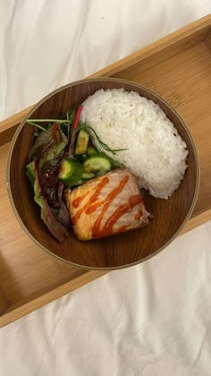 a wooden tray with rice, meat and vegetables on it next to a glass of water