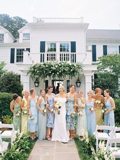 a group of women standing next to each other in front of a white house with flowers