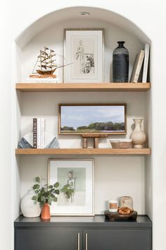 a shelf with pictures, vases and other items on it in a room that has white walls