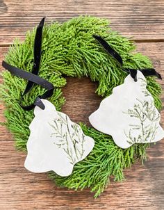 a wreath with two white ornaments hanging from it's side on top of a wooden table