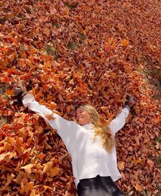 a woman laying on top of a pile of leaves in the middle of a field