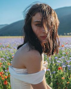 a woman standing in a field of flowers with her hair blowing back and looking at the camera