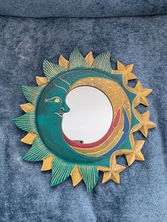 a sun mirror sitting on top of a blue velvet covered bed sheet with gold stars around it