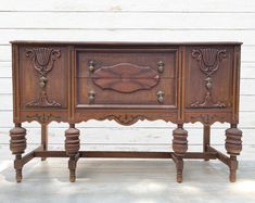 an old wooden sideboard with ornate carvings on the front and sides, sitting against a white wall