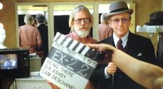 two men in suits and hats are holding a movie clapper while another man is pointing at the camera