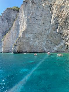 several boats floating in the blue water next to a large rock formation with cliffs on either side