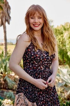 a woman with red hair is standing in front of some palm trees and smiling at the camera