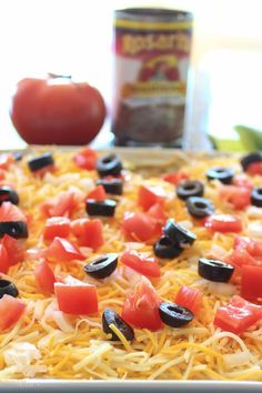 a pizza with olives, tomatoes and cheese in a baking pan next to an apple