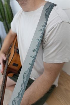 a man sitting on the floor with a guitar strap around his neck and wearing a white t - shirt