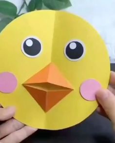 someone holding up a paper cut out of a yellow bird with big eyes and nose