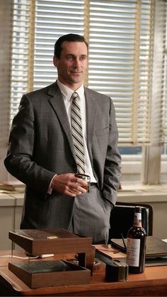 a man in a suit and tie standing next to a desk with bottles on it