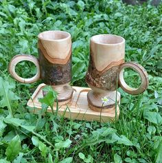 two wooden mugs sitting on top of a wooden tray in the middle of some grass