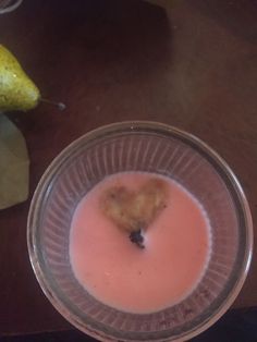 a glass bowl filled with pink liquid next to a banana on a wooden table top