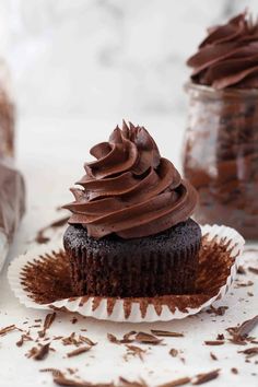 a chocolate cupcake with frosting on a plate next to two jars of chocolate shavings